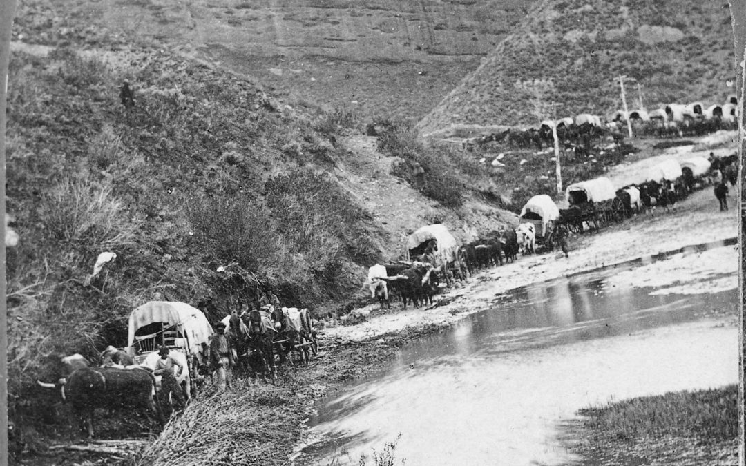 A black and white photo of a covered wagon on a river.